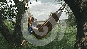 Relaxed young man reading book in hammock. Relax in hammock. Man resting on weekend in countryside. Male lying in hammock and enjo