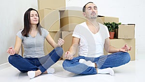 Relaxed young man and woman relaxing together in new house, meditating with positive thoughts, practicing yoga in lotos