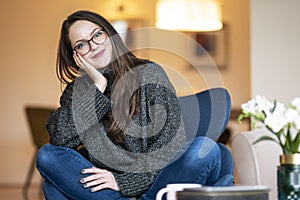 Relaxed young woman with beautiful smile sitting on the chair in the living room