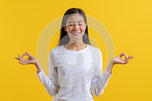 Relaxed young woman in casual white shirt meditate isolated on yellow background