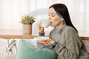 Relaxed young woman enjoying aromatic coffee at home