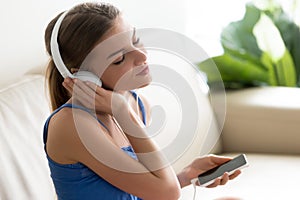 Relaxed young woman enjoying music in headphones using mobile ap