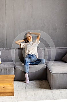 Relaxed young woman feel fatigue lounge on comfortable sofa hands behind head rest at home, happy calm lady dream enjoy wellbeing