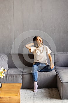 Relaxed young woman feel fatigue lounge on comfortable sofa hands behind head rest at home, happy calm lady dream enjoy wellbeing