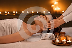 Relaxed young woman getting head massage at romantic spa atmosphere