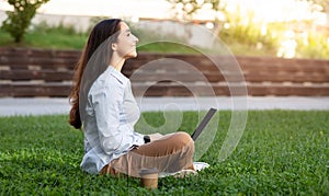 A relaxed young woman with long hair, wearing a blue shirt and brown trousers, sits back and enjoys a break