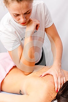 Relaxed young woman lying face down on massage table enjoying therapeutic body massage by professional masseur in spa or wellness