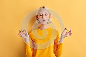 Relaxed young woman meditating with eyes closed  over yelow background