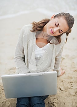 Relaxed young woman sitting on lonely beach with laptop