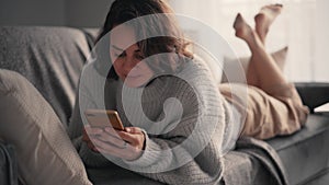 A relaxed young woman using her smartphone while lying on the sofa.