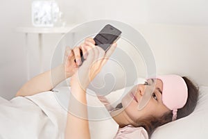 Relaxed young woman using a smartphone in the morning on the bed at home. Happy and smiling girl using a mobile phone