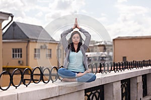 Relaxed young woman in a yoga pose on the parapet