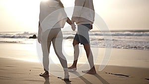 Relaxful couple walking barefoot on the beach.They are spending time together, leaving footprints on wet sand, holding