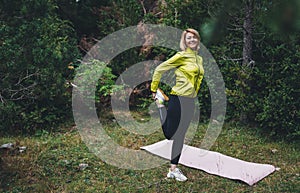 Relaxing activity with stretch arms and legs. Young fit woman doing stretching exercises  training outside in green park