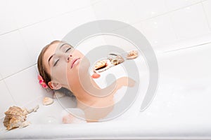 Relaxing attractive young woman lying in the bath with foam, enjoying spa relaxation treatment eyes closed