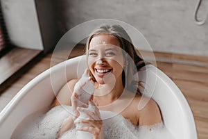 Relaxing bath. Happy lady lying in bathtub, enjoying beauty ritual, looking and smiling at camera, copy space