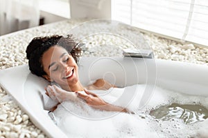 Relaxing bath. Happy young woman lying in bathtub with closed eyes, enjoying beauty ritual at luxury spa, copy space