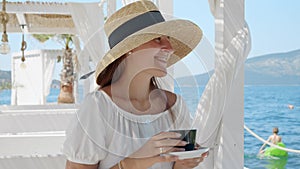 Relaxing at a beach cafe, a young brunette sips coffee, eyes on the sea waves. Capturing summer holidays, vacation