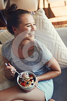 Relaxing with a bowl of muesli. an attractive young woman eating her breakfast while relaxing on the sofa at home.