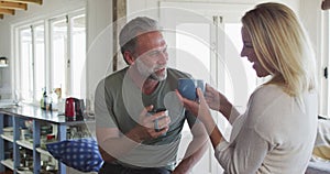 Relaxing caucasian mature couple drinking coffee and talking in kitchen