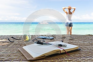 Relaxing girl, opened empty notepad is on the table with sunglasses, phone and headphones at the tropical sea background