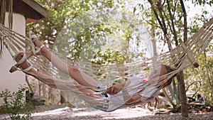 Relaxing girl swinging in hammock at summer vacation. Teenager girl relaxing in hammock in summer garden on trees