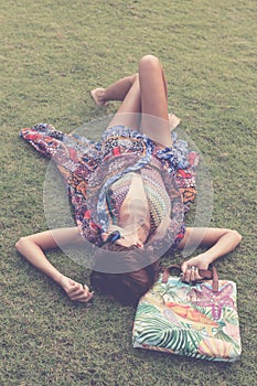 Relaxing in grass. Top view of beautiful young woman in sunglasses and pareo lying on the green grass with beach bag in