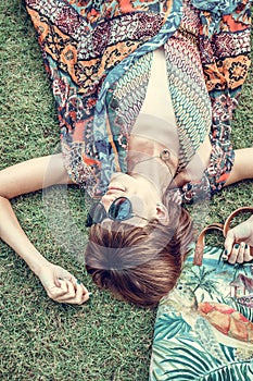 Relaxing in grass. Top view of beautiful young woman in sunglasses and pareo lying on the green grass with beach bag in