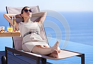Relaxing while on holiday. A posh young woman reclining on a deck chair with her hands behind her head.