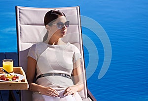 Relaxing while on holiday. A posh young woman sitting on a deck chair by the poolside.