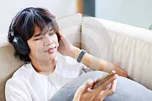 Relaxing at Home, Asian Male Enjoying Music and Using Smartphone