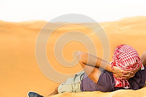 Relaxing male tourist lying on top of a desert hill with his hands behind head.