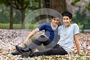 Relaxing outdoors together. Cute young gay Asian couple smiling together while sitting in the park.