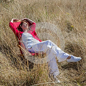 Relaxing 50s woman enjoying sun warmth alone on her deckchair