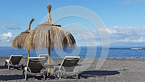 Relaxing spot on the pebble beach of Playa de la Enramada with two thatched umbrellas and four chaise lounges