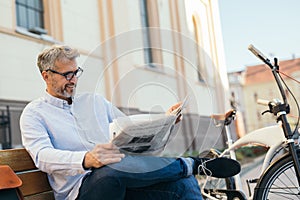 Relaxing time in city. man reading newspaper in city , bicycle in blurred background