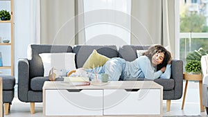 Relaxing, tired young girl going to sleep on sofa at home. Female getting comfort from a couch in a living room and