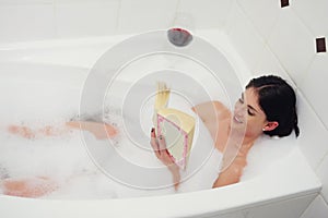 Relaxing in the tub. Cropped shot of a young woman relaxing in the bathtub with a book and glass of wine.