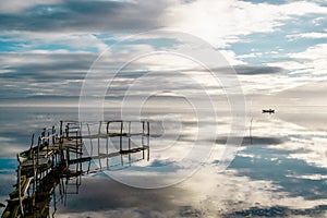 Relaxing view of a reflected blue sky with clouds, a ramshackle wharf and a fishing boat.