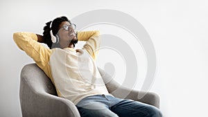 Relaxing Weekend. Happy Black Millennial Guy In Wireless Headphones Resting In Chair