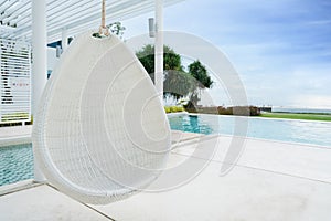 Relaxing white rattan hanging chair at swimming pool on sea view