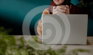 Relaxing and Working via Computer Laptop at Home or Cafe. Smiling Woman holding a Cup of Hot Tea