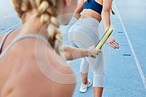 Relay race athlete handing the baton over to a teammate while running from behind. Rearview closeup of two female