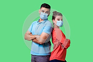 Reliable friendship. Cheerful young couple of friends with surgical medical mask standing back to back with crossed hands and