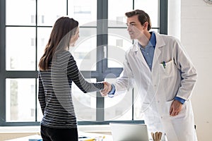 Reliable physician and female patient shaking hands before consultation