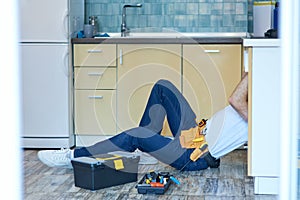 Reliable service. Professional repairman, plumber examining and fixing sink pipe in the kitchen