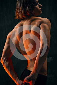 Relief, muscular, athletic male back. Shirtless model with fit body posing against dark studio background