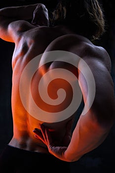 Relief, muscular, athletic male back. Shirtless model with fit body posing against dark studio background