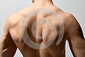 Relief, strong, muscular back. Male model posing shirtless  over light grey studio background. Cropped photo
