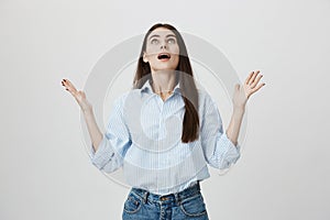 Relieved and gladful young european female raising hands and looking up with opened mouth and satisfied expression